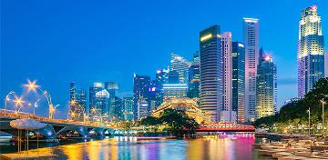 Die Skyline des Finanzdistrikts von Singapur spiegelt sich farbig im Wasser.