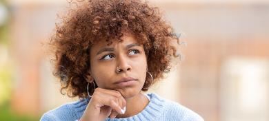 Eine junge Frau mit lockigen Haaren blickt nachdenklich nach oben.