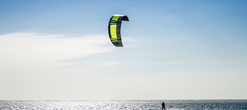 Ein Kitesurfer surft im Meer vor blauem Himmel.