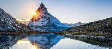 Die tiefstehende Sonne und ein schneebedeckter Berg spiegeln sich in einem See in den Schweizer Alpen.